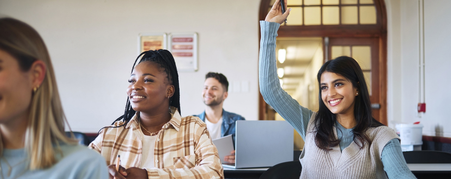 Student in classroom smiling with hand raised