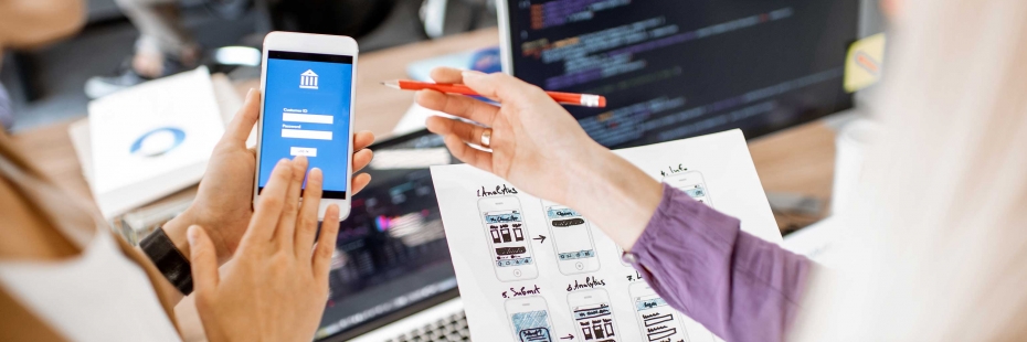 two collaborators working on a mobile user interface with coding screens in the background